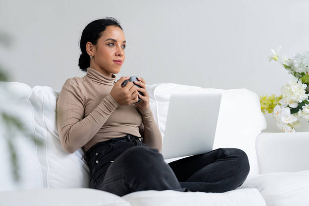 Szczęśliwa kobieta pijąca kawę na kanapie w domu dla odpoczynku i relaksu. Portret młodej Afroamerykanki trzymającej filiżankę. - Zdjęcie, obraz