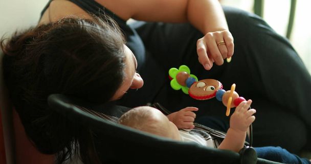Candid mamá interactuando con el bebé recién nacido jugando con juguete en silla - Foto, imagen