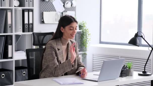 Boldog kaukázusi üzletasszony kezében egy videohívás segítségével laptop, miközben dolgozik papírok ül az íróasztal a modern irodai környezetben. - Felvétel, videó