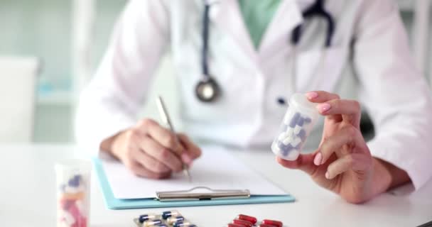 Therapist medicine cardiologist doctor holds jar of pills and writes out prescription to patient. Choice of drug and selection of drug for disease - Footage, Video