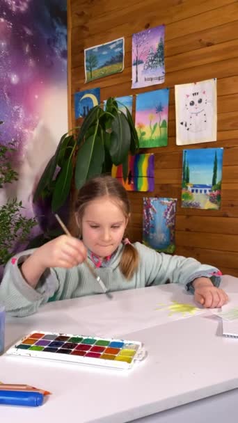 Espressione artistica giovanile, hobby d'infanzia. Verticale di una bella bambina si impegna nella pittura ad acquerello, esplorando la sua creatività e immaginazione sullo sfondo di disegni e piante d'appartamento al chiuso - Filmati, video