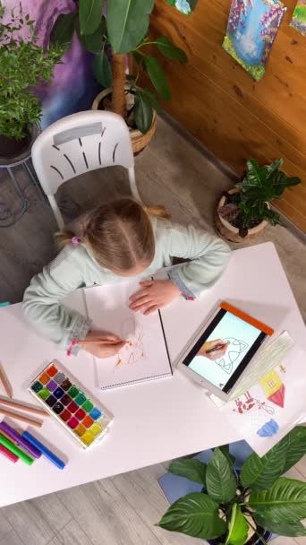 Çevrimiçi evde eğitim, çocukluk hobisi. Güzel küçük bir kızın dikey görüntüsü dijital tablet kullanarak kapalı alanda resim yapmayı öğrendiği bir video dersini izliyor. Yaratıcılık, sanatsal beceriler geliştirme - Video, Çekim