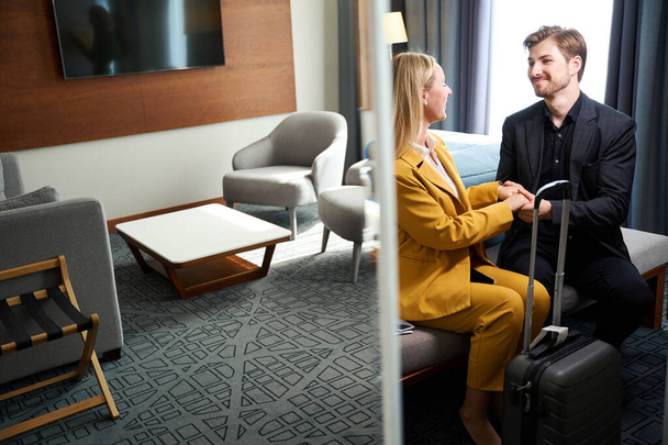 Un hombre y una mujer se registraron en una habitación de hotel, personas con trajes de viaje y con una maleta - Foto, Imagen