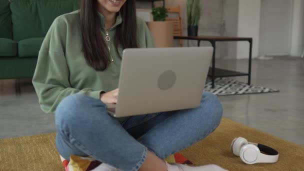 Una mujer joven utiliza el ordenador portátil en casa mientras se sienta cómodo - Metraje, vídeo