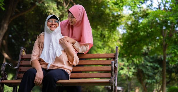 Μουσουλμάνος προσεκτικός φροντιστής ή νοσηλευτής που φροντίζει τον ασθενή στο νοσοκομειακό πάρκο. Ευτυχισμένη Μουσουλμάνα με μαντίλα που αγκαλιάζει την κόρη. Έννοια της αποταμίευσης και Senior Ασφάλισης Υγείας, μια ευτυχισμένη οικογένεια - Φωτογραφία, εικόνα