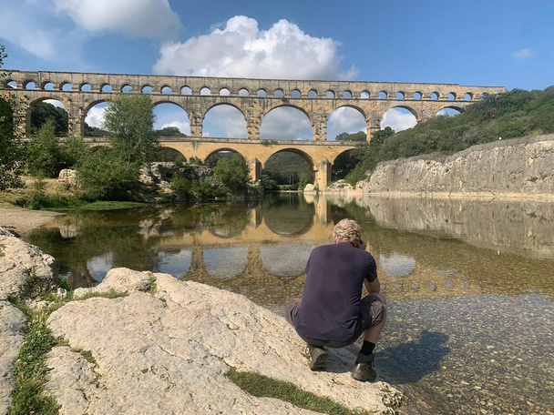 Ο άνθρωπος κάθεται κοντά στην αρχαία ρωμαϊκή Pont du Gard υδραγωγείο και γέφυρα viaduct, η υψηλότερη από όλες τις αρχαίες ρωμαϊκές γέφυρες, κοντά στο Nimes στη Νότια Γαλλία. - Φωτογραφία, εικόνα