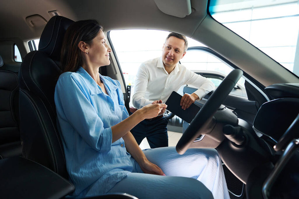 Autoliikkeen johtaja esittelee uuden auton asiakkaalle, nainen istuu kuljettajan istuimella - Valokuva, kuva