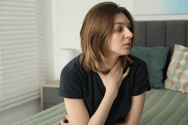 Sad young woman sitting on bed at home - Photo, image