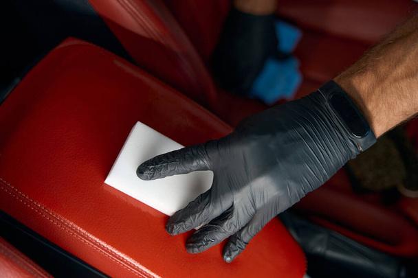 Nettoyage d'un accoudoir en cuir avec une éponge en mélamine, un homme travaillant dans des gants de protection - Photo, image