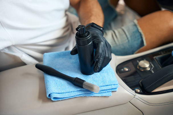 Persoon gebruikt een speciaal reinigingsschuim, een zachte doek en een borstel om de binnenkant van een auto schoon te maken - Foto, afbeelding