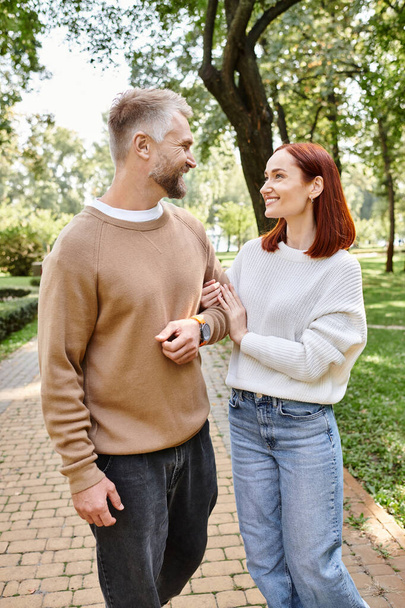 Un uomo e una donna stanno fianco a fianco su un sentiero di mattoni in un parco. - Foto, immagini
