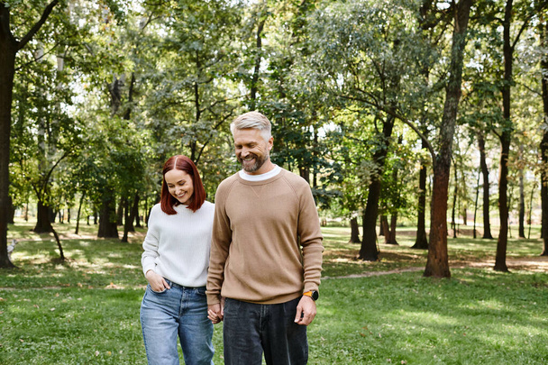 Ein erwachsenes Paar in legerer Kleidung spaziert gemütlich durch einen ruhigen Park. - Foto, Bild