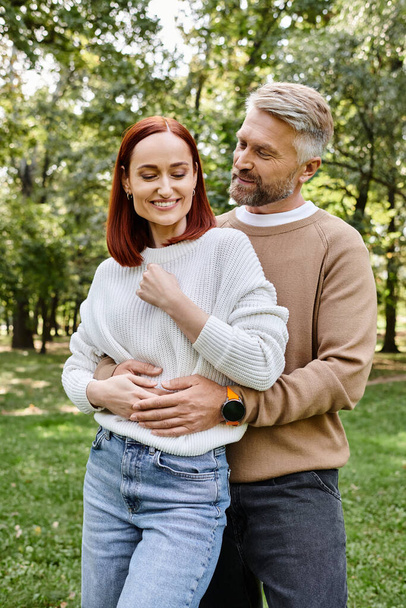 Una coppia di adulti innamorati in abbigliamento casual in piedi nel parco erboso. - Foto, immagini
