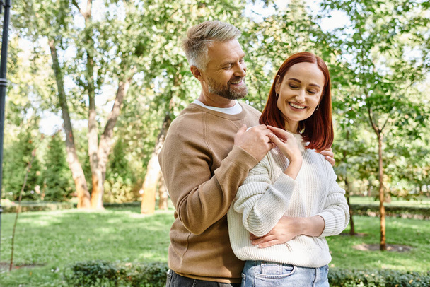 A loving couple in casual attire stands together in a park. - Photo, Image