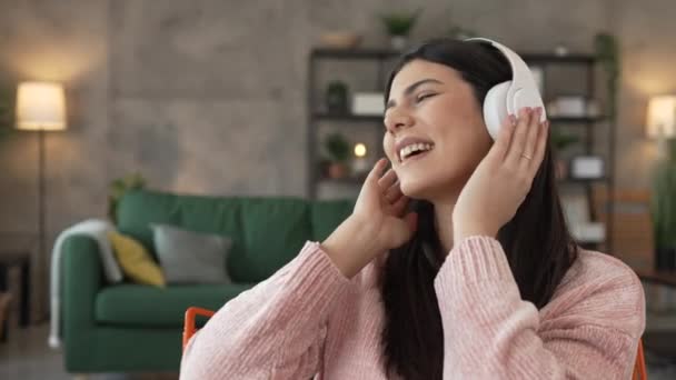 ヘッドフォンを持つ1人の白人女性大人の女性は,音楽を聞くために自宅で携帯電話を使用する オンライン幸せな笑顔歌の喜びは,単独のスローモーションを持っています - 映像、動画