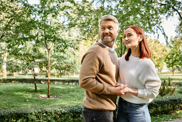 Una coppia in abbigliamento casual si trova insieme in un parco, godendo di una piacevole passeggiata. - Foto, immagini