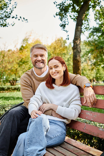 Volwassen echtpaar in casual kleding genieten van een rustig moment op een park bank. - Foto, afbeelding
