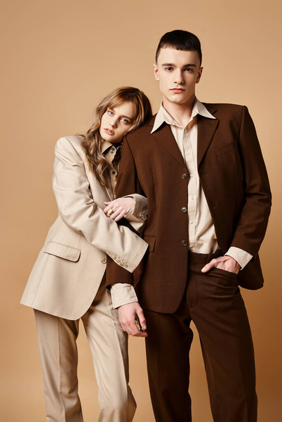 alluring elegant couple in debonair suits posing together and looking at camera on pastel backdrop - 写真・画像