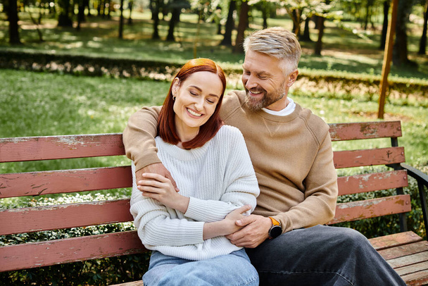 Ένας άντρας και μια γυναίκα απολαμβάνουν μια ήρεμη στιγμή σε ένα παγκάκι στο πάρκο.. - Φωτογραφία, εικόνα