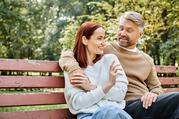 Ein liebevolles erwachsenes Paar in Freizeitkleidung sitzt zusammen auf einer Parkbank. - Foto, Bild