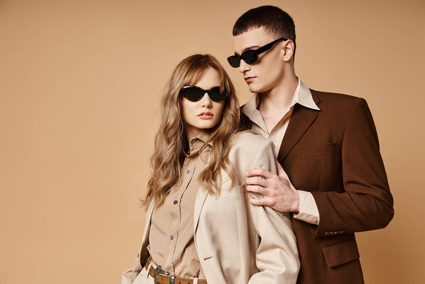 alluring elegant couple in chic seasonal suits with stylish sunglasses posing on pastel background - Φωτογραφία, εικόνα