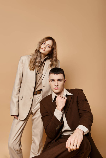 appealing couple in sophisticated suits posing together and looking at camera on pastel backdrop - 写真・画像