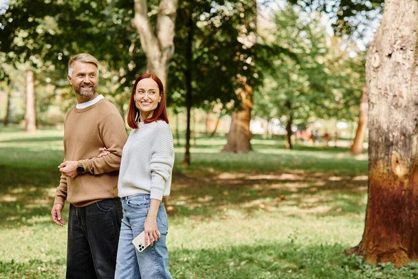 Un hombre y una mujer en atuendo casual se paran uno al lado del otro en un exuberante parque. - Foto, imagen