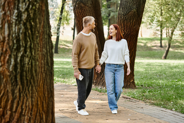 Una coppia, vestita con disinvoltura, cammina mano nella mano in un parco. - Foto, immagini