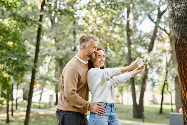 Kochająca się para uchwyca chwilę w parku, kiedy robią sobie razem selfie. - Zdjęcie, obraz