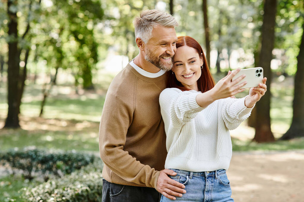 Um homem e uma mulher de traje casual tirando uma selfie em um parque. - Foto, Imagem