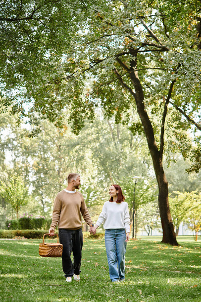 Mężczyzna i kobieta w stroju casual trzymając się za ręce, spacerując po parku. - Zdjęcie, obraz