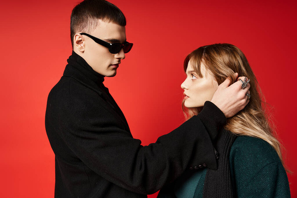 good looking young woman and her boyfriend with sunglasses looking at each other on red backdrop - Foto, Imagen