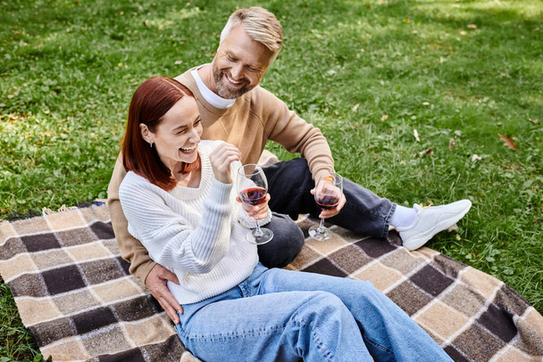 Mann und Frau sitzen zusammen auf einer Decke und halten Weingläser in der Hand. - Foto, Bild
