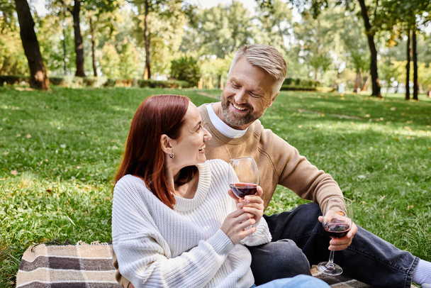 Kadın ve erkek battaniyeye oturmuş, ellerinde şarap kadehleriyle dışarıda romantik bir anın tadını çıkarıyorlar.. - Fotoğraf, Görsel