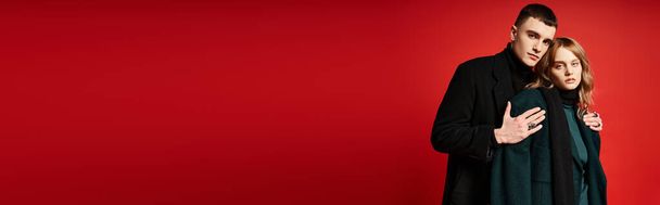 junges Liebespaar in edlen Mänteln blickt in die Kamera auf rotem, lebendigem Hintergrund, Banner - Foto, Bild