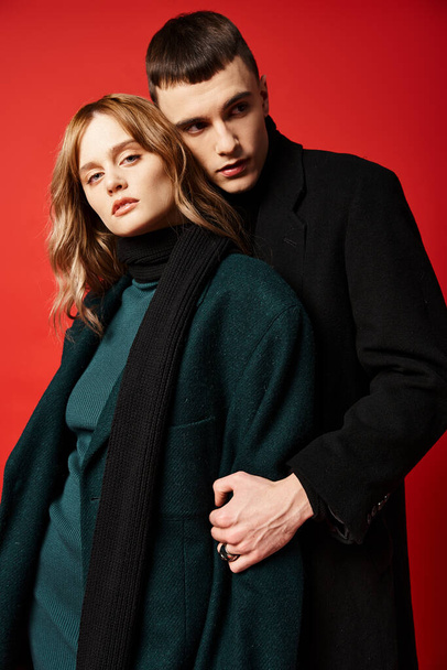 appealing woman in coat looking at camera and posing lovingly with her boyfriend on red backdrop - Foto, Imagem