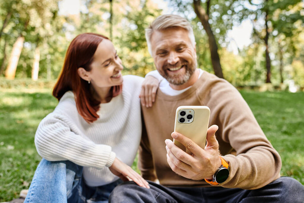 Un couple qui s'amuse en compagnie tout en regardant un téléphone portable sur l'herbe. - Photo, image