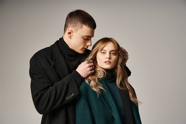 good looking stylish boyfriend and girlfriend in coats posing lovingly together on gray backdrop - Фото, изображение