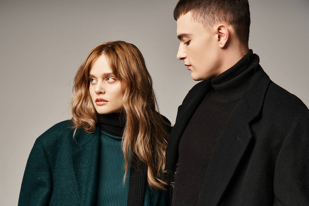 good looking girlfriend and boyfriend in chic coats posing and looking away on gray background - Zdjęcie, obraz