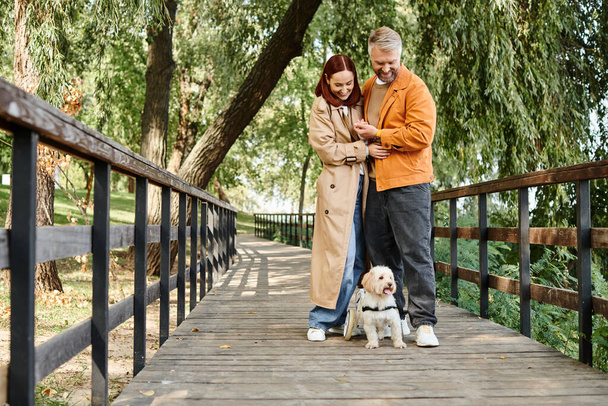 Coppia adulta e cane in piedi insieme su un ponte in un parco. - Foto, immagini