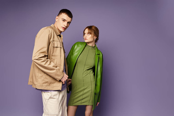appealing young woman in green jacket looking lovingly at her handsome boyfriend on purple backdrop - Zdjęcie, obraz