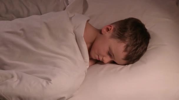 kleine jongen gooit rusteloos in slaap op een kussen onder een deken 's nachts. Slapen kleuter kind zoon op een bed in de slaapkamer in de avond - Video