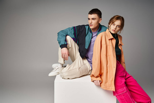 alluring woman in fashionable bomber looking at camera next to her handsome boyfriend on white cube - Photo, Image