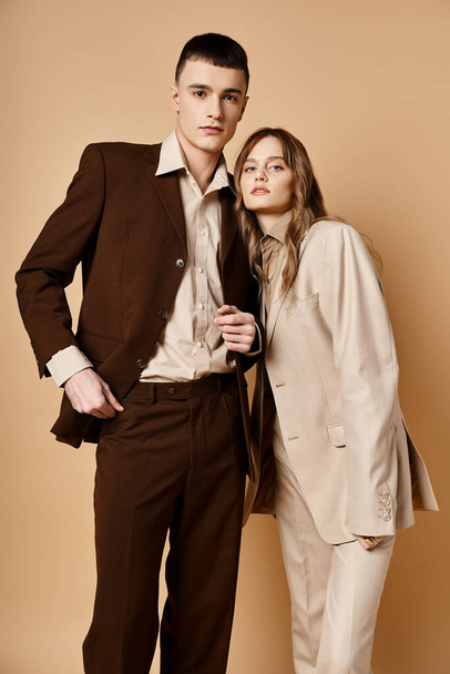 verleidelijk trendy paar in stijlvolle pakken poseren op pastel achtergrond en kijken naar de camera - Foto, afbeelding