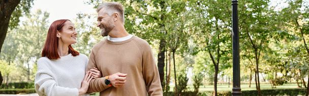 Un amorevole coppia adulta in abbigliamento casual camminare insieme attraverso un parco sereno. - Foto, immagini