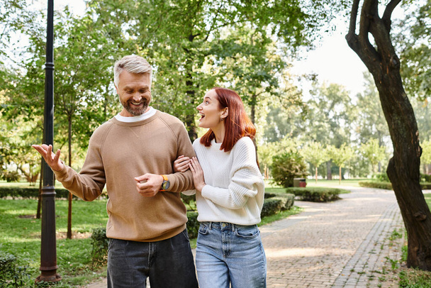 Una pareja adulta cariñosa con atuendo casual caminando por una acera en un parque. - Foto, imagen