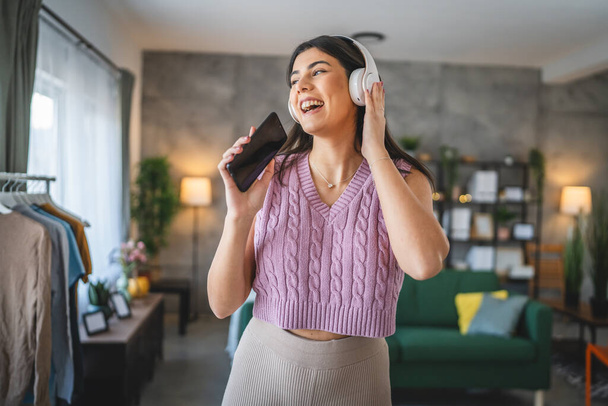 One caucasian woman adult female with headphones use mobile phone at home to listen to the music online happy smile sing joy have fun alone - Photo, Image