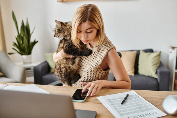 A woman with short hair sits at a table, contently petting her cat perched on her lap, creating a serene atmosphere. - Photo, Image
