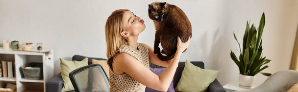 Eine Frau mit kurzen Haaren hält ihre Katze dicht vor ihrem Gesicht und teilt einen Moment der Liebe und Verbundenheit zu Hause. - Foto, Bild