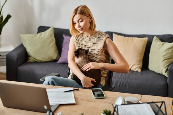 Une femme aux cheveux courts s'assoit sur un canapé, tenant un chat dans un moment serein de convivialité à la maison. - Photo, image